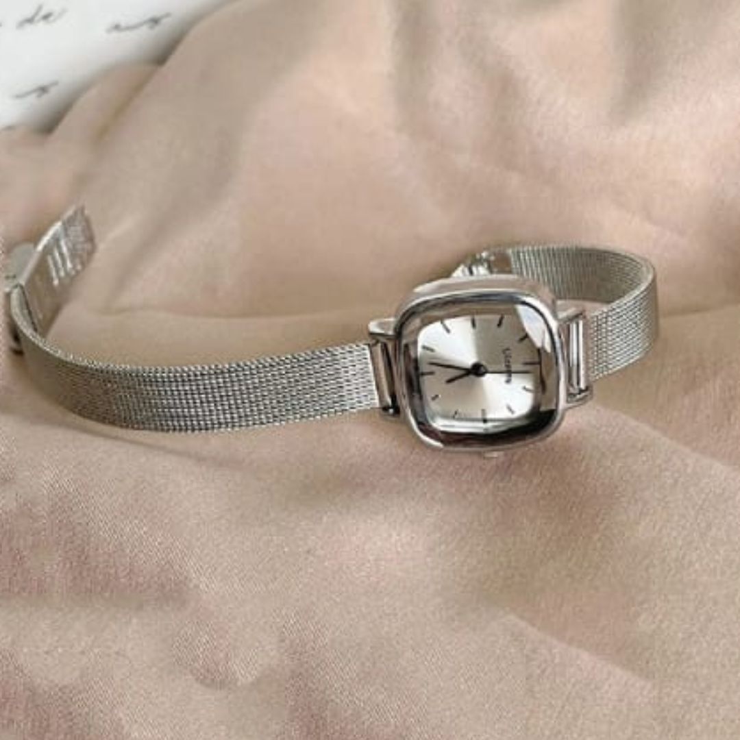 Silver watch with mesh band on a beige surface