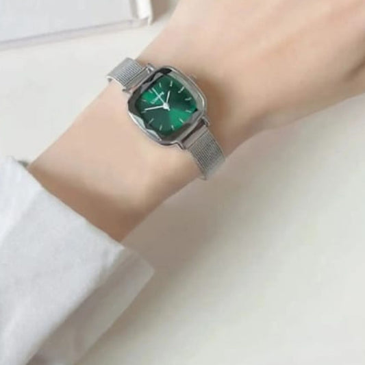 Wrist wearing a silver watch with a green face on a white background